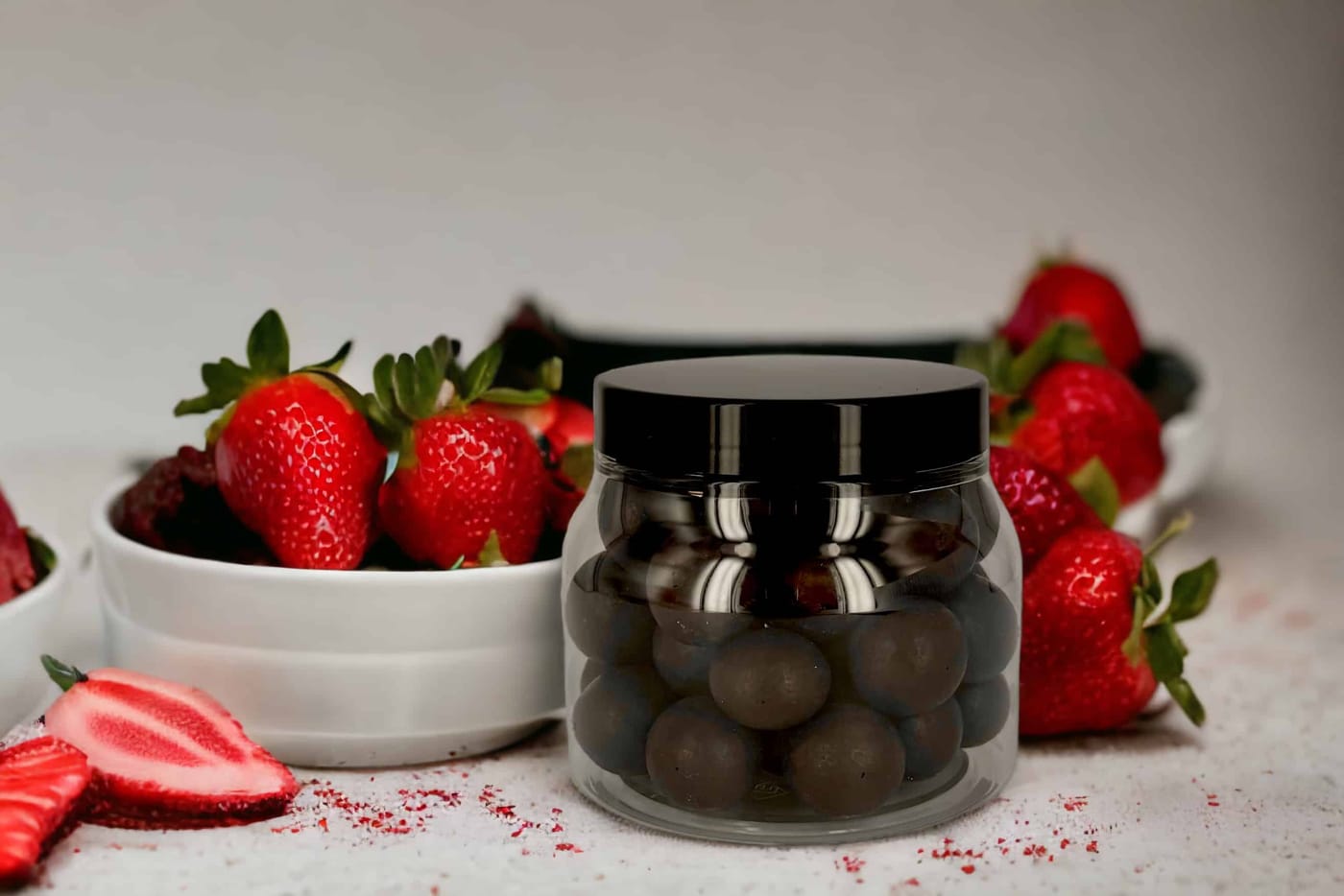 Chocolate pralines in a clear PET jar with a black lid, next to fresh strawberries
